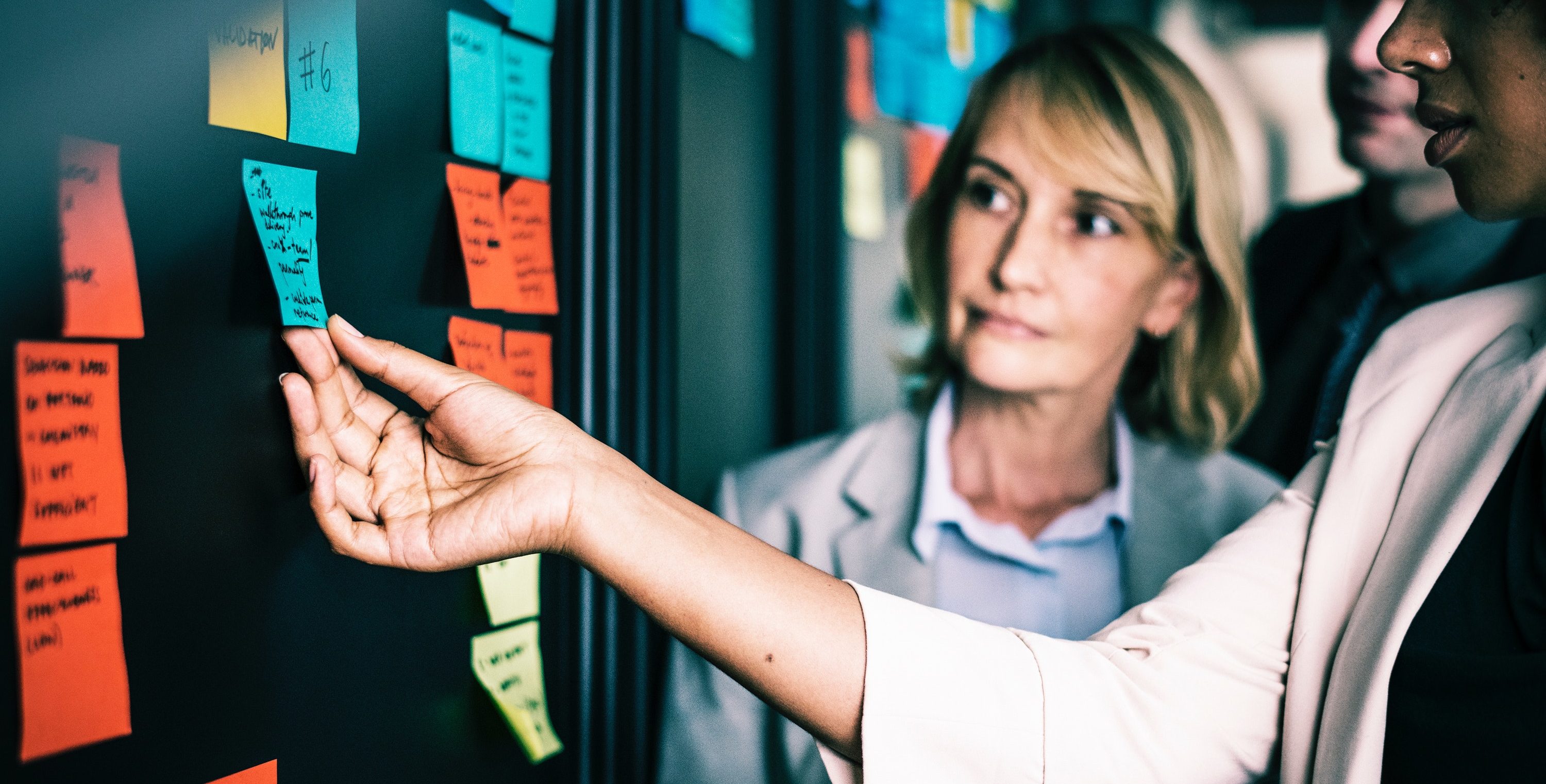 Women pinning a post-it note to the wall in an office