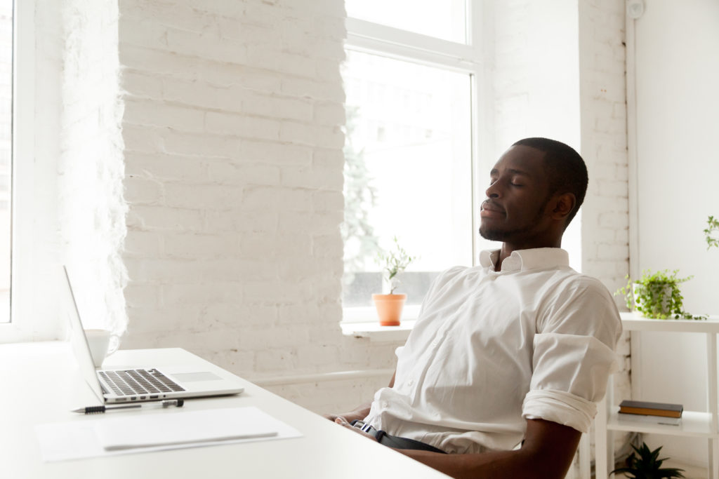 A man sits calmly at his desk with his eyes closed.