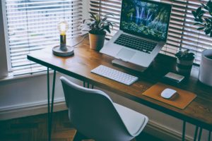 An attractive home office setup that includes a laptop on a stand, a desk lamp and plants.