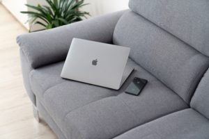 A laptop and phone sit on an empty couch.