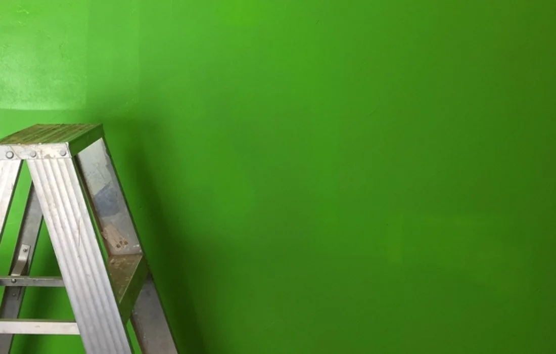 A ladder with a paint lid and brush sits against a freshly-painted wall.