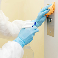 Close up of a worker wearing gloves while disinfecting an elevator button