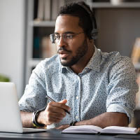 A man takes notes while working at a laptop.