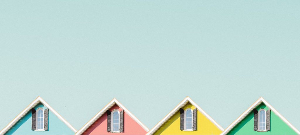 The tops of a row of brightly-coloured houses sit against a light blue background.