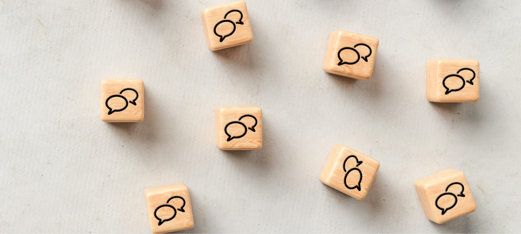 Game piece cubes engraved with images of speech bubbles sit on a plain surface.
