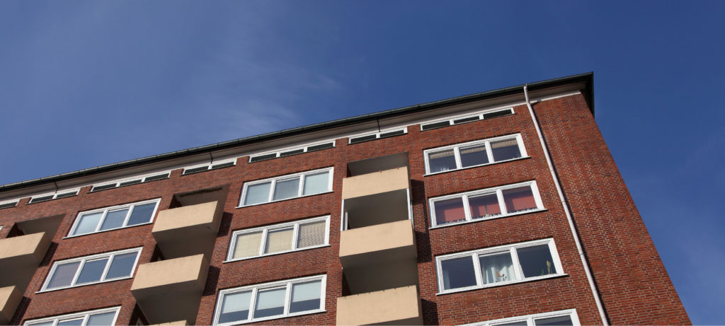 View from the ground up of an apartment building against a blue sky.