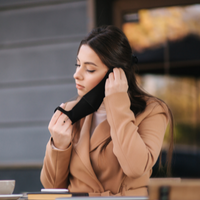 Woman sitting at a table outside putting on a black face mask