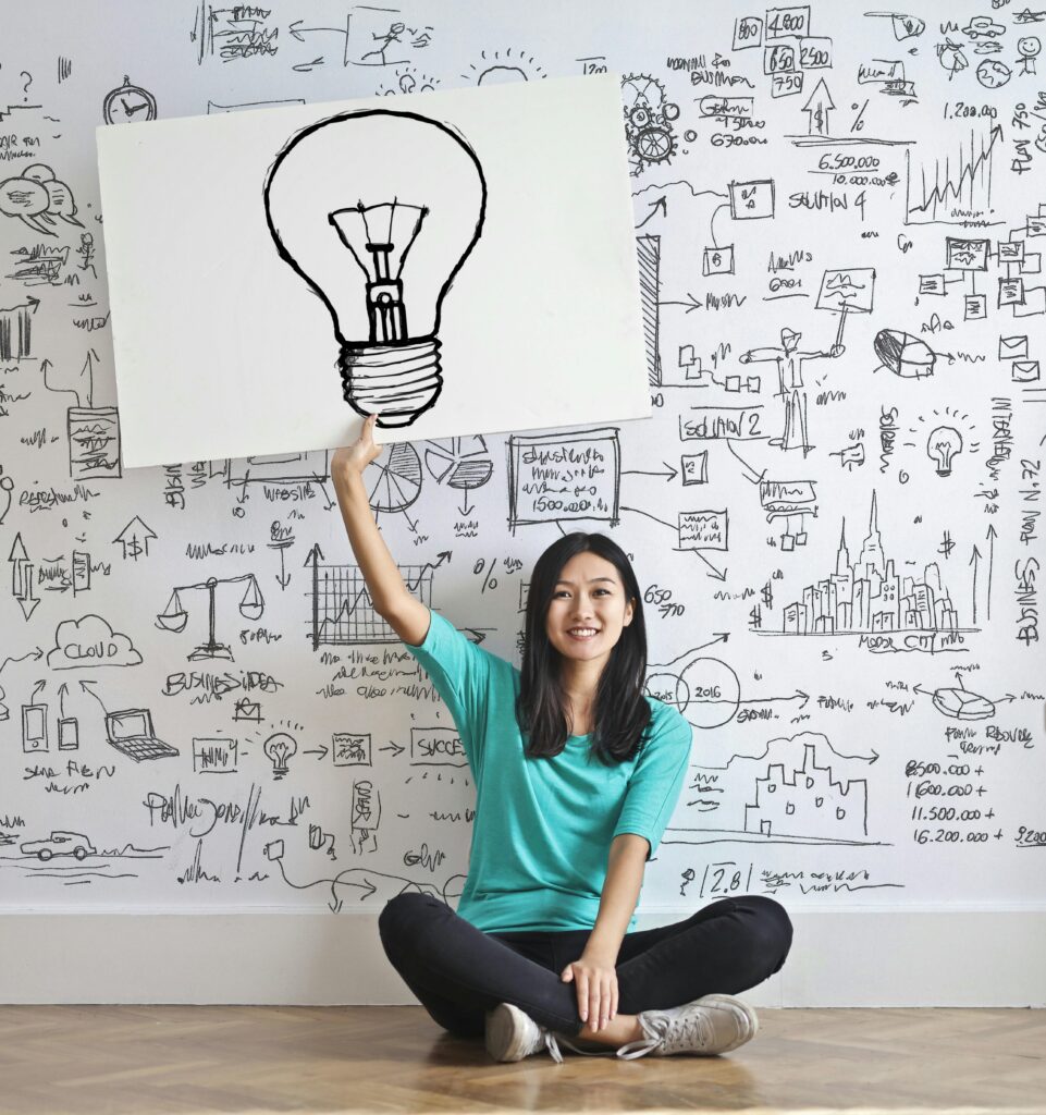 Image of a girl sitting on the floor and holding a sign of a lightbulb